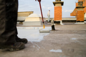 Low angle view of the worker putting the primer of the hydro isolation on the roof of high building